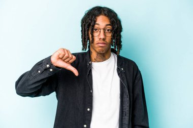 Genç Afro-Amerikan bir adam mavi arka planda izole edilmiş, hoşlanmadığı bir jest gösteriyor, başparmakları aşağıda. Anlaşmazlık konsepti.