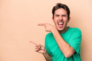 Beyazlı genç adam bej arka planda izole edilmiş. İşaret parmaklarıyla işaret ettiği için heyecanlı..