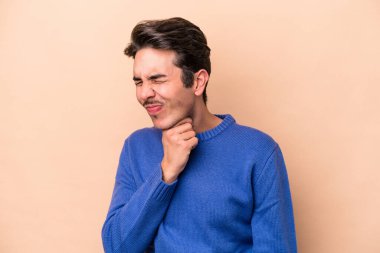 Beyazlı genç bir adam bej arka planda virüsten ya da enfeksiyondan boğaz ağrısı çekiyor..