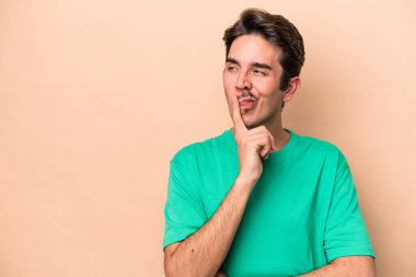 Beyazlı genç adam bej arka planda izole edilmiş şüpheli ve şüpheci bir ifadeyle yana bakıyor..