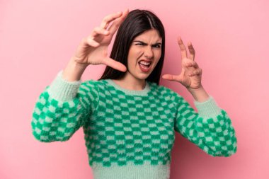 Pembe arka planda izole edilmiş genç beyaz kadın gergin elleriyle çığlık atıyor..