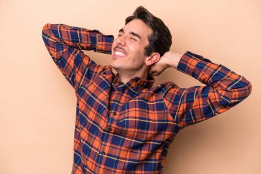 Beyazlı genç bir adam bej arka planda izole edilmiş. Kendine güveniyor, elleri başının arkasında..