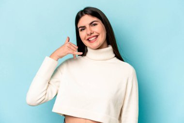 Mavi arka planda izole edilmiş genç beyaz kadın parmaklarıyla bir cep telefonu hareketi gösteriyor..