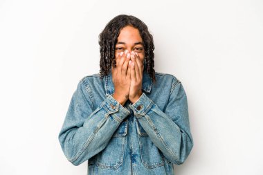 Genç Afro-Amerikalı bir adam beyaz arka planda izole edilmiş bir şekilde bir şeylere gülüyor, elleriyle ağzını kapatıyor..
