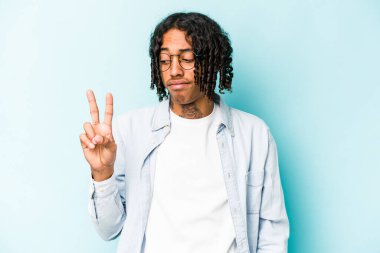 Genç Afrikalı Amerikalı adam mavi arka planda izole edilmiş neşeli ve kaygısız parmakları olan bir barış sembolü gösteriyor..