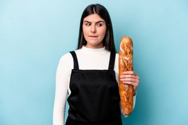 Genç fırıncı Kafkas elinde mavi arka planda izole edilmiş bir somun ekmek tutuyor. Kafası karışmış ve kendinden emin değil..