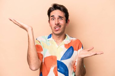 Kafkasyalı genç adam bej arka planda izole edilmiş. Kafası karışmış ve omuz silkiyor. Kopya alanını tutmak için..