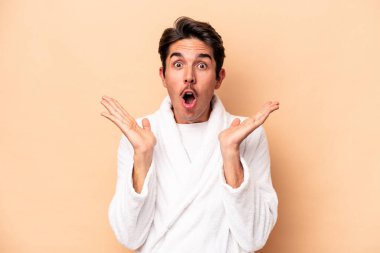 Kafkasyalı genç bir adam bej arka planda izole edilmiş, şaşırmış ve şok olmuş..