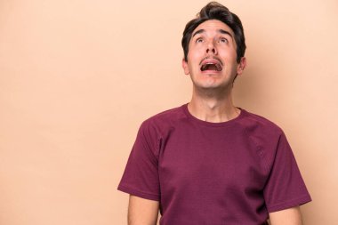 Beyazlı genç bir adam bej arka planda izole edilmiş çok kızgın, öfkeli, hayal kırıklığına uğramış.