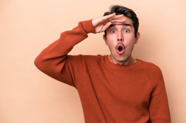 Beyaz tenli genç adam bej arka planda izole edilmiş yüksek sesle bağırıyor, gözleri açık ve elleri gergin tutuyor..