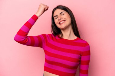 Pembe arka planda izole edilmiş genç beyaz kadın zaferi, tutkuyu ve coşkuyu kutluyor, mutlu bir ifade..