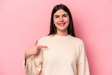 Pembe arka planda izole edilmiş genç beyaz bir kadın gömlek fotokopisini elle gösteriyor, gururlu ve kendinden emin.