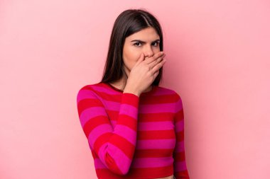 Pembe arka planda izole edilmiş genç, beyaz bir kadın elleri endişeli bir şekilde ağzı örtüyor..