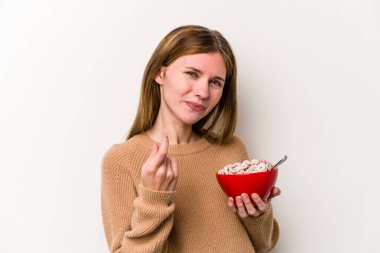 Beyaz arka planda yalıtılmış mısır gevreği yiyen genç İngiliz kadın sanki seni davet ediyormuş gibi seni işaret ediyor..