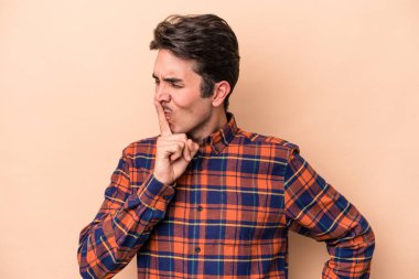 Beyazlı genç bir adam bej arka planda izole edilmiş bir şekilde sır saklıyor ya da sessizlik istiyor..