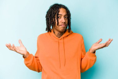 Genç Afrikalı Amerikalı adam mavi arka planda izole edilmiş sorgulama jestinde şüphe ediyor ve omuz silkiyor..