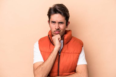 Beyaz tenli genç adam bej arka planda izole edilmiş düşünüyor ve yukarı bakıyor, yansıtıyor, düşünüyor, bir fantezi kuruyor..