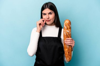 Genç fırıncı Kafkasyalı, mavi arka planda izole edilmiş bir somun ekmek tutuyor ve parmakları dudaklarında bir sır saklıyor..
