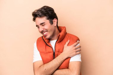 Beyaz tenli genç adam bej arka planda izole edilmiş gülüyor ve eğleniyor..