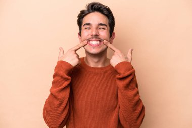 Beyazların arka planında izole edilmiş genç beyaz adam gülümsüyor, parmaklarını ağzına doğrultuyor..