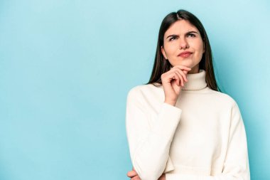 Mavi arka planda soyutlanmış beyaz bir kadın şüpheli ve şüpheci bir ifadeyle yana bakıyor..