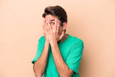 Beyazlı genç bir adam bej arka planda izole edilmiş. Korkmuş ve gergin parmaklarıyla göz kırp..