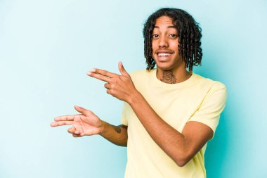 Genç Afro-Amerikalı adam mavi arka planda izole edilmiş. İşaret parmaklarıyla işaret ederek heyecanlı..