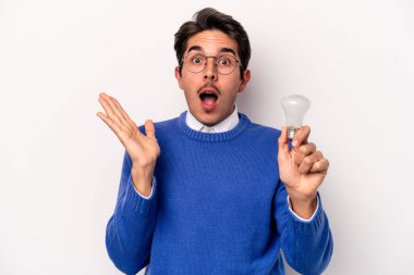 Beyaz arka planda izole edilmiş bir ampul tutan genç beyaz adam şaşırdı ve şok oldu..