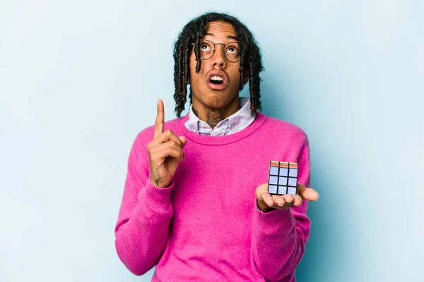 Mladý Afroameričan Drží Kostku Rubiks Izolované Modrém Pozadí Ukazuje Vzhůru — Stock fotografie