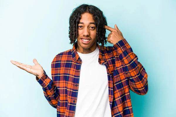 Genç Afrikalı Amerikalı bir adam mavi arka planda izole edilmiş ve elinde bir ürün tutuyor..