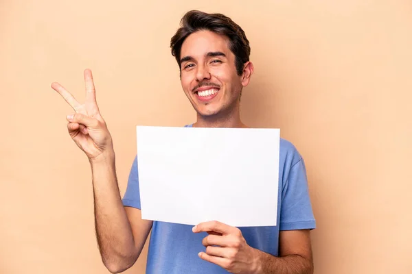 ベージュ地にプラカードを持つ若い白人男性喜びと屈託のない指で平和のシンボルを示す — ストック写真