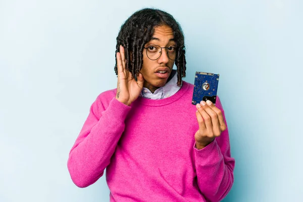 Young African American informatic man isolated on blue background trying to listening a gossip.