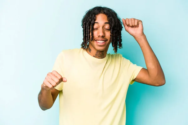 Young African American man isolated on blue background celebrating a special day, jumps and raise arms with energy.