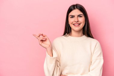 Pembe arka planda izole edilmiş genç beyaz kadın işaret parmağıyla işaret ederek gülümsüyor..