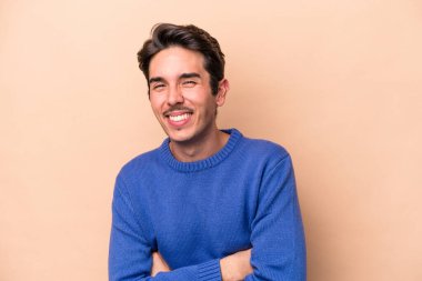 Beyaz tenli genç adam bej arka planda izole edilmiş gülüyor ve eğleniyor..