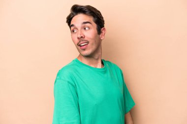 Beyaz tenli, bej arka planda izole bir genç. Gülümsüyor, neşeli ve keyifli görünüyor..