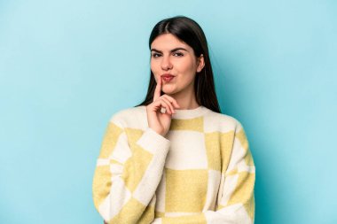 Kafkasyalı genç bir kadın, mavi arka planda izole edilmiş. Bir strateji planlıyor, bir işin nasıl olacağını düşünüyor..