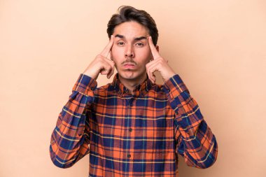 Beyazlı genç bir adam bej arka planda izole edilmiş bir vazifeye odaklanmış, işaret parmaklarını işaret ediyor..