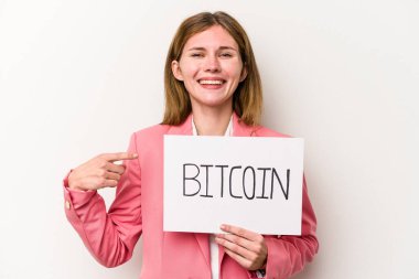 Beyaz arka planda izole edilmiş Bitcoin pankartı tutan genç İngiliz iş kadını gülümsüyor ve boş alanda bir şeyler gösteriyor..