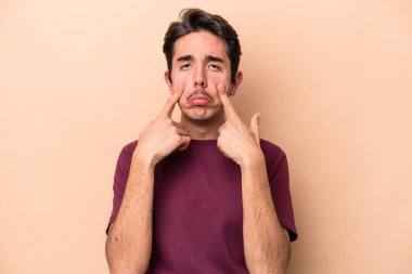 Beyaz tenli genç adam bej arka planda izole edilmiş ağlıyordu, bir şeyden mutsuzdu, ıstırap ve kafa karışıklığı vardı..