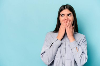 Kafkasyalı genç bir kadın mavi arka planda izole edilmiş düşünceli bir şekilde ağzıyla ağzını kapatan bir fotokopi odasına bakıyor..