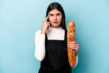 Genç fırıncı Kafkas elinde mavi arka planda izole edilmiş bir somun ekmek tutuyor. Şakağı parmağıyla işaret ediyor, düşünüyor ve bir göreve odaklanıyor..