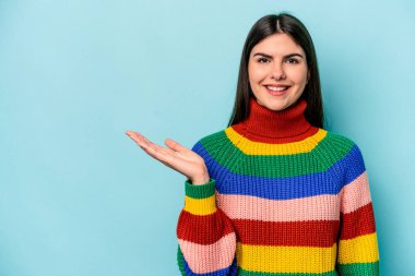 Mavi arka planda izole edilmiş genç beyaz kadın bir avuç içinde fotokopi alanı ve belinde bir el daha gösteriyor..