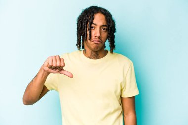 Genç Afro-Amerikan bir adam mavi arka planda izole edilmiş, hoşlanmadığı bir jest gösteriyor, başparmakları aşağıda. Anlaşmazlık konsepti.
