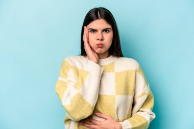 Mavi arka planda izole edilmiş genç beyaz kadın yanakları patlatıyor, yorgun bir ifadesi var. Yüz ifadesi kavramı.