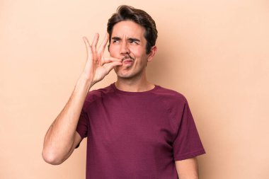 Beyazlı genç bir adam bej arka planda izole edilmiş ve parmakları dudaklarında bir sır saklıyor..