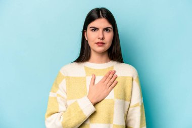 Beyaz bir kadın mavi arka planda izole edilmiş yemin ediyor, elini göğsüne koyuyor..