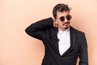 Kafkasyalı genç koruma bej arka planda izole edilmiş kafasının arkasına dokunuyor, düşünüyor ve bir seçim yapıyor..