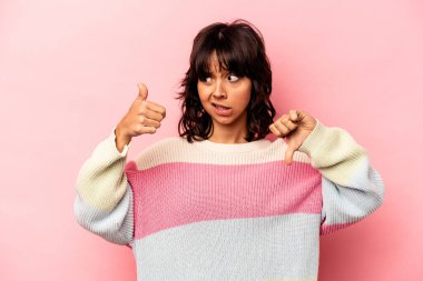 Pembe arka planda izole edilmiş genç İspanyol kadın baş parmağını kaldırıyor, zor seçim konsepti.