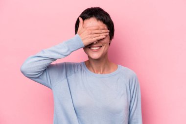 Pembe arka planda soyutlanmış beyaz bir kadın elleriyle gözlerini kapatıyor, büyük bir gülümsemeyle bir sürpriz bekliyor..